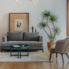 Modern gray sofa with a plush texture, paired with a green table, against a light wooden floor and neutral wall decor.