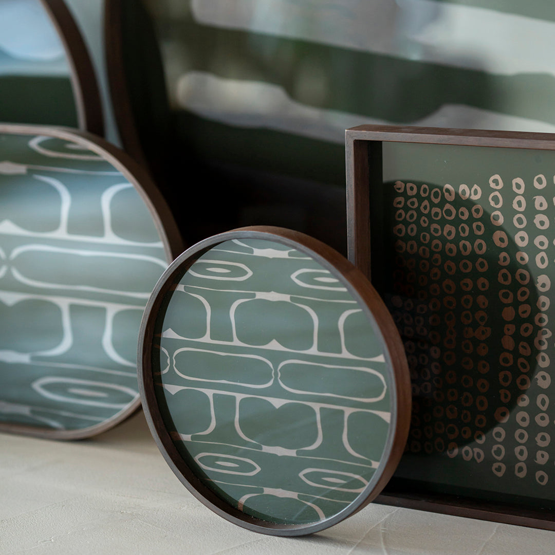 Round and rectangular trays featuring green geometric patterns and rich brown frames. Modern decor accents.