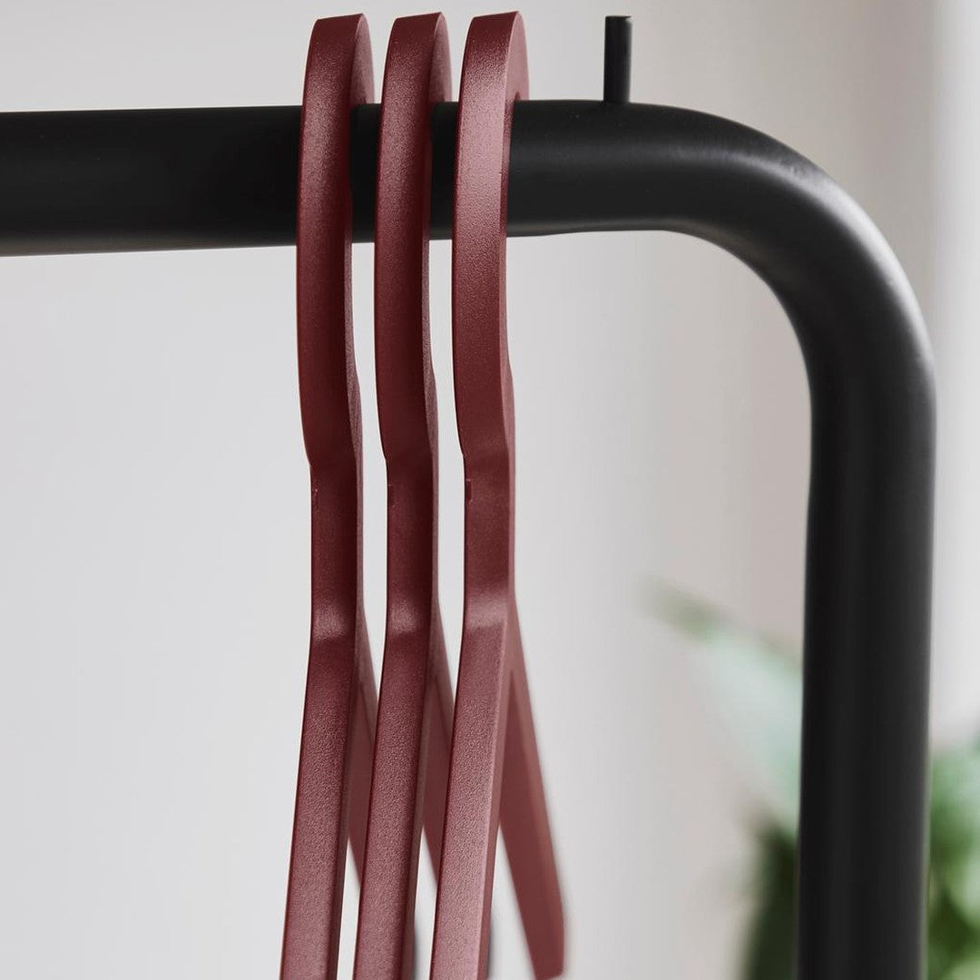 Red metallic hangers on a black rack against a soft, light background, creating a modern, minimalistic aesthetic.