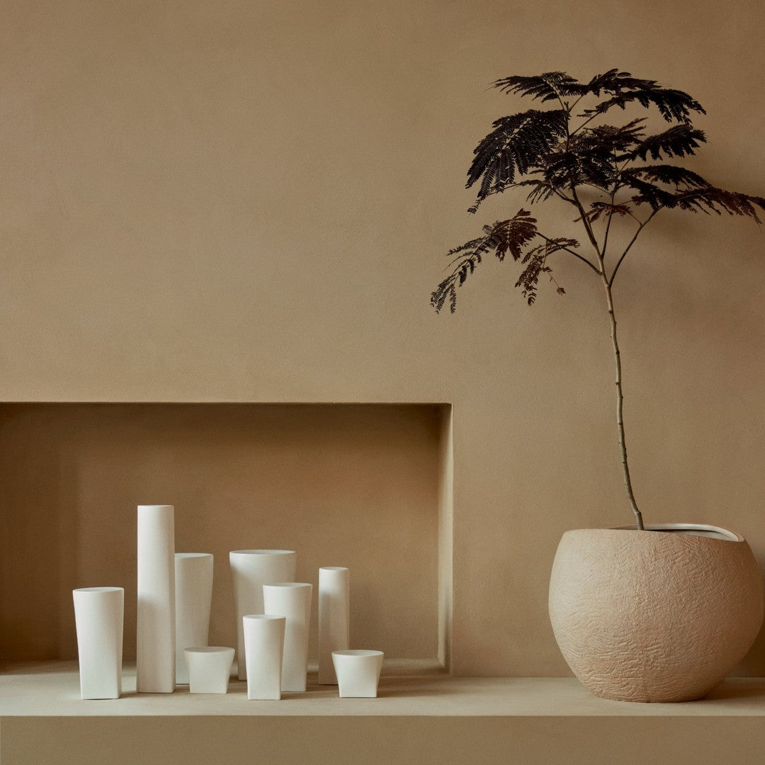 White ceramic vases in various shapes against a warm, neutral background with a minimalist design.