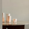 Soft white cylindrical lanterns on a marble table against a muted gray background, creating a calm, elegant ambiance.