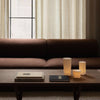 Brown sofa with soft texture, elegant beige curtains, and minimalistic white and beige candle holders on a wooden table.