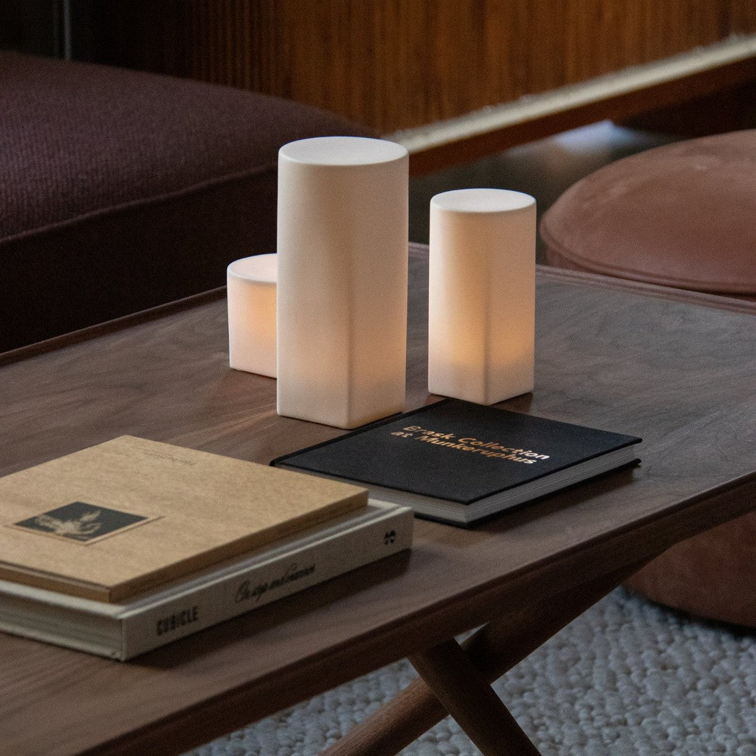 Soft white cylindrical lamps on a wooden table with neutral-toned books and a textured surface.