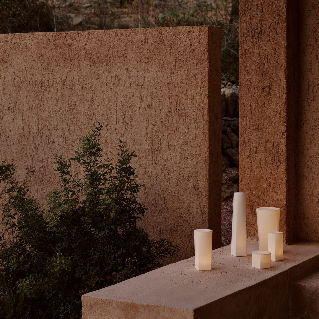 "Neutral-toned cylindrical candles on a textured stone backdrop with green foliage for a serene ambiance."
