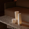 White geometric candle holders on a textured stone table, with warm ambient lighting, in a cozy living room setting.