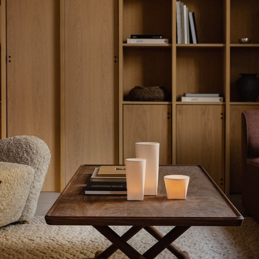 Elegant wooden table with neutral-toned candles and books, featuring warm beige and light brown hues in a cozy setting.