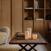 Elegant wooden table with neutral-toned candles and books, featuring warm beige and light brown hues in a cozy setting.