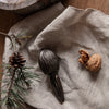 Rustic brown nutcracker on textured beige fabric with green pine needles and pinecone accents.