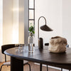 Black round table with a textured white vase, clear glass accents, and modern black lamp, featuring neutral wall tones.