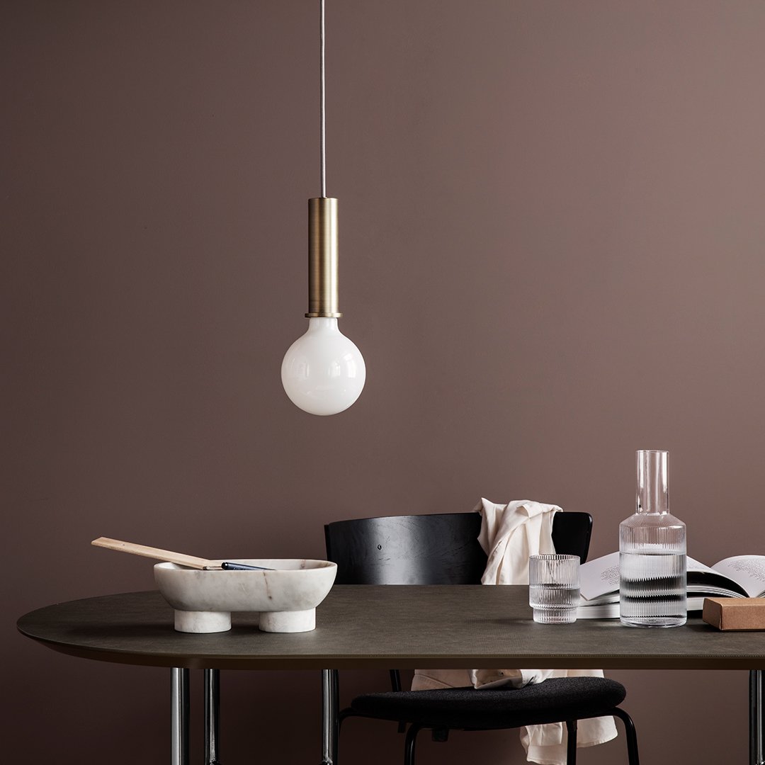 Modern pendant light with a matte white bulb and sleek gold metal accents against a rich brown backdrop.