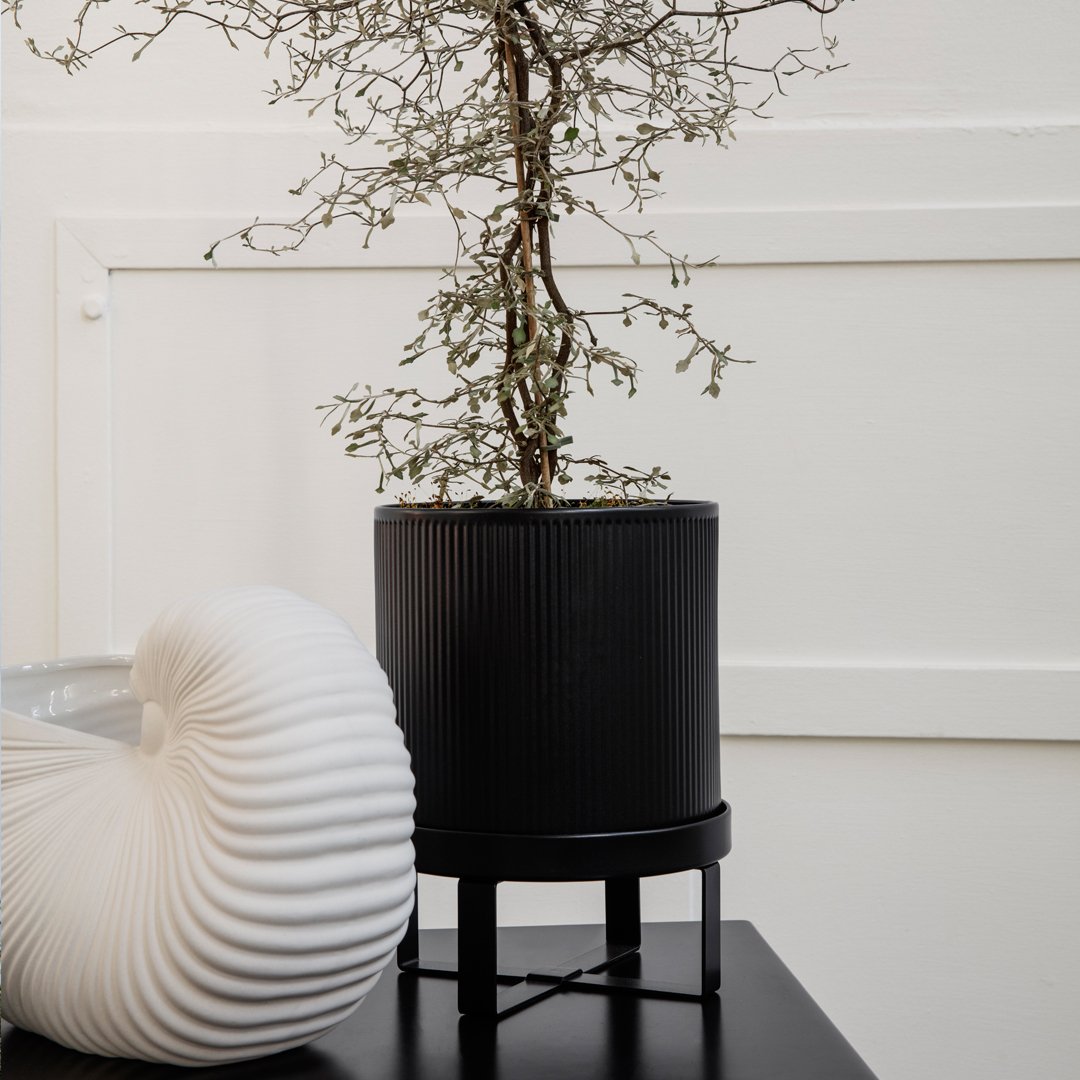 Black ribbed planter with a minimalist design and a textured white decorative object beside it. Modern, neutral colors.