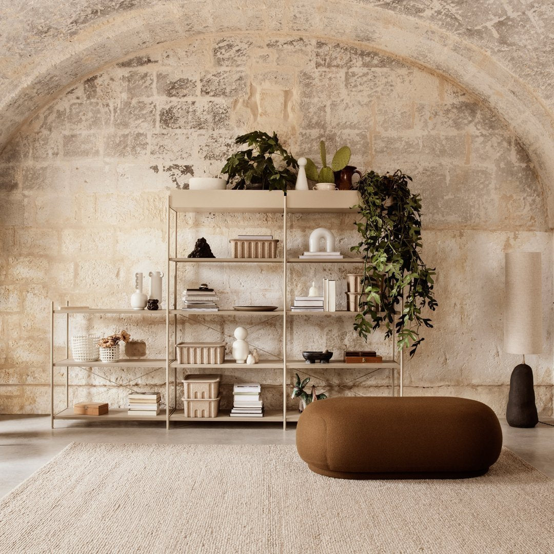 Modern shelving unit with soft gold accents, earthy brown pouf, and natural stone wall backdrop featuring green plants.