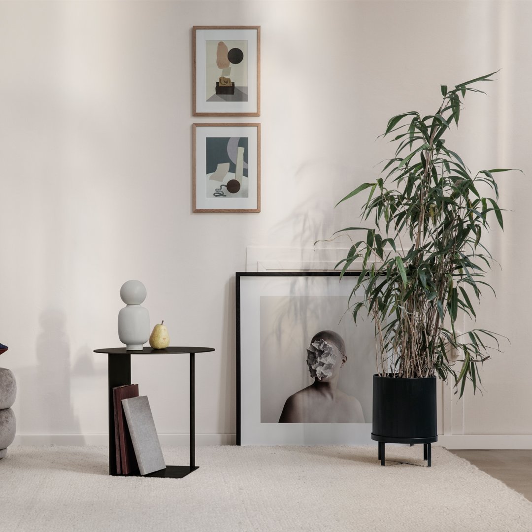 Black side table with geometric design, surrounded by neutral walls and colorful framed artwork in a modern room.