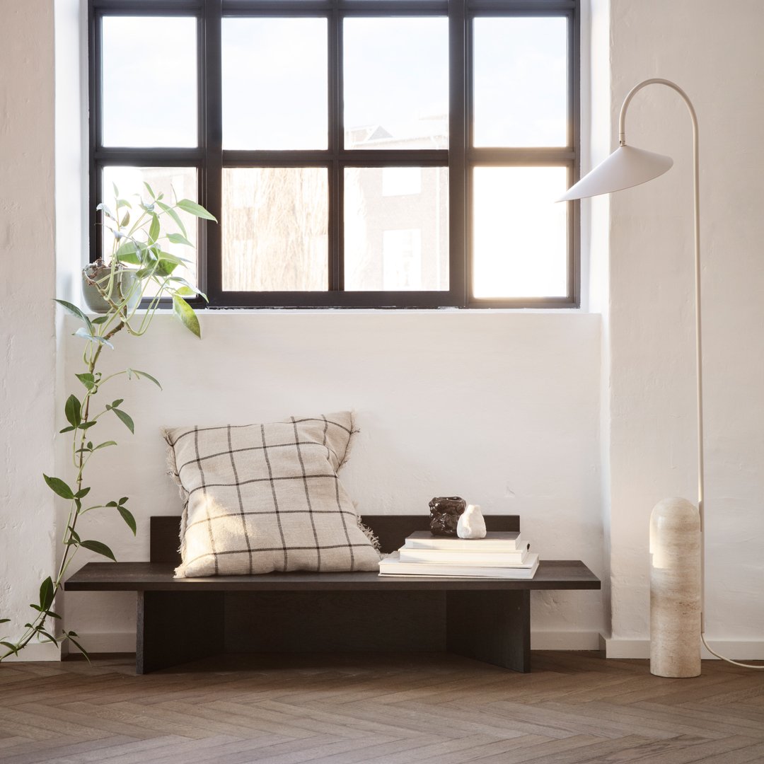 "Neutral-toned bench with a black and white plaid pillow, surrounded by natural greenery and warm wooden accents."