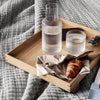 Wooden tray with textured gray blanket, clear striped glassware, and a crumpled beige napkin with a golden croissant.