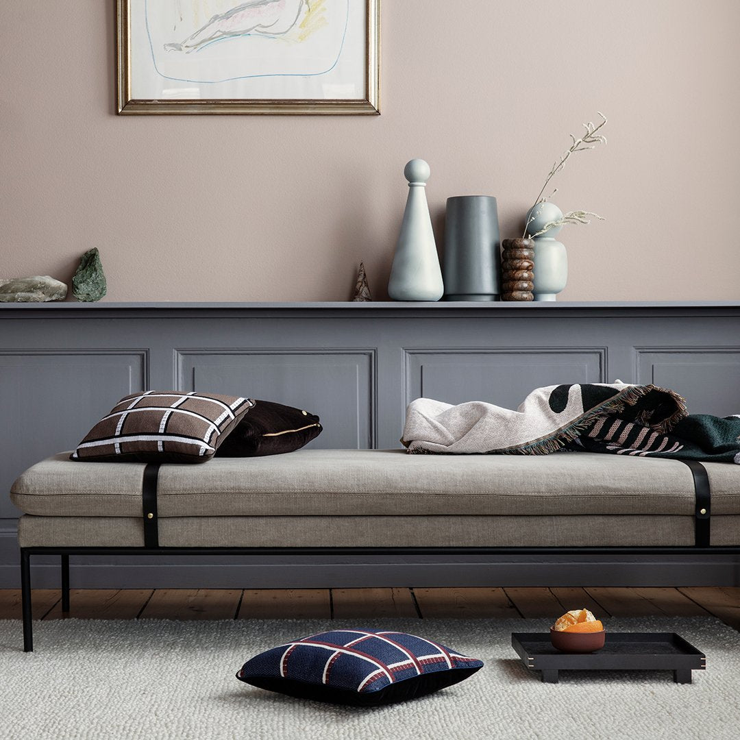 Neutral gray daybed with patterned black and white pillows, dark blue plaid cushion, and pastel decor accents.