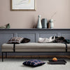 Neutral gray daybed with patterned black and white pillows, dark blue plaid cushion, and pastel decor accents.