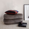 Gray plush ottoman stacked with a multi-colored striped pillow featuring red, blue, and black accents.