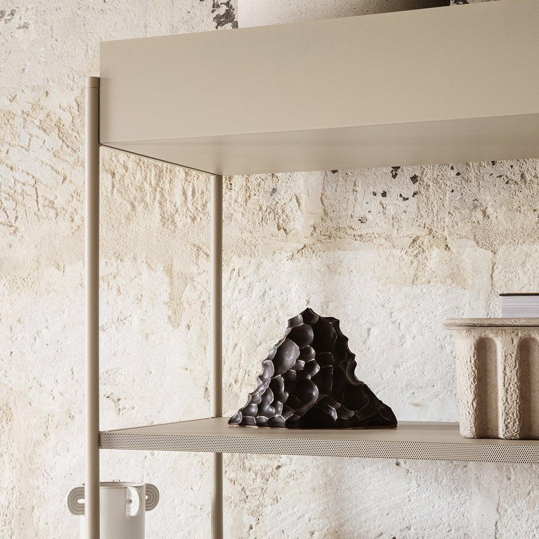 Beige shelf with a textured black sculpture on a light, rough stone background. Elegant and minimalist design.