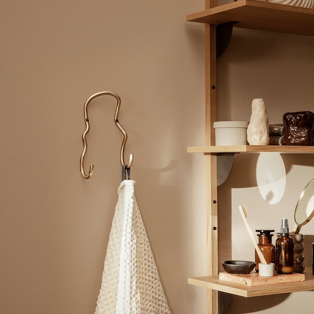 Sleek gold wall hook against a warm taupe backdrop, paired with a textured cream towel for a stylish, modern look.