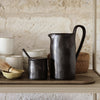 Black ceramic pitcher and small jar with a smooth, matte finish, set against a light neutral backdrop.