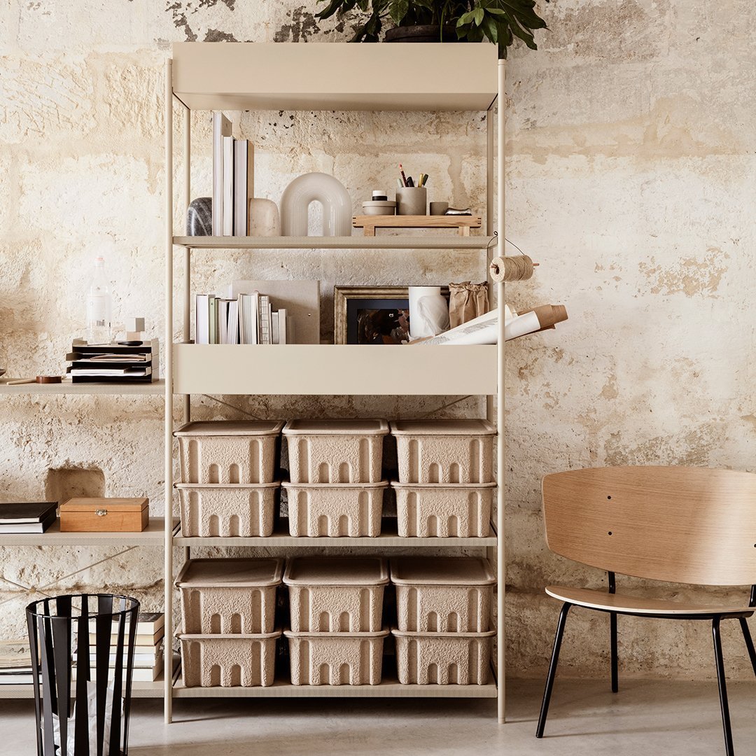 Beige shelving unit with a minimalist design, featuring multiple light tan storage bins and a textured neutral wall backdrop.