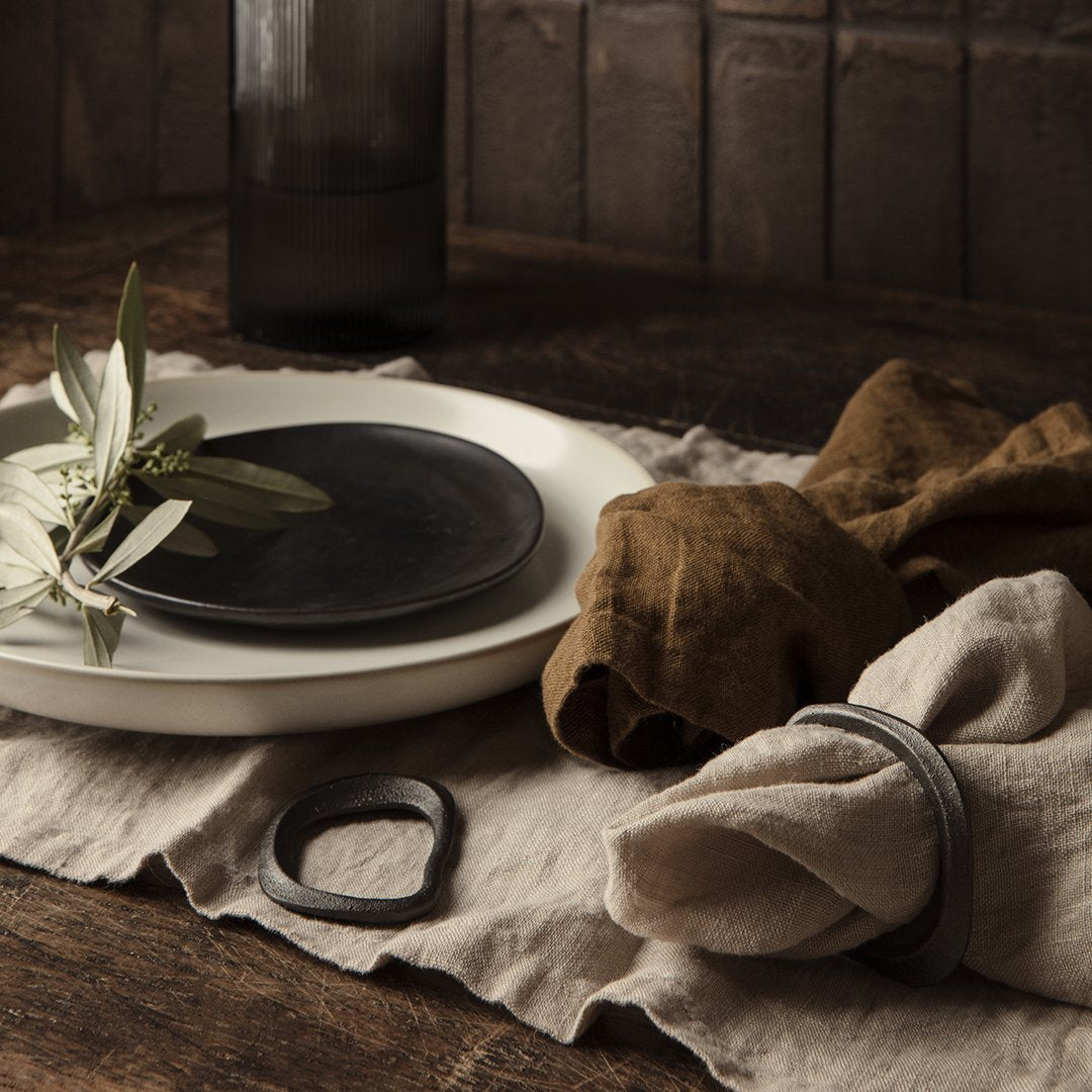 Black and white dinnerware with earthy linen napkins on a textured table. Natural elements enhance rustic charm.