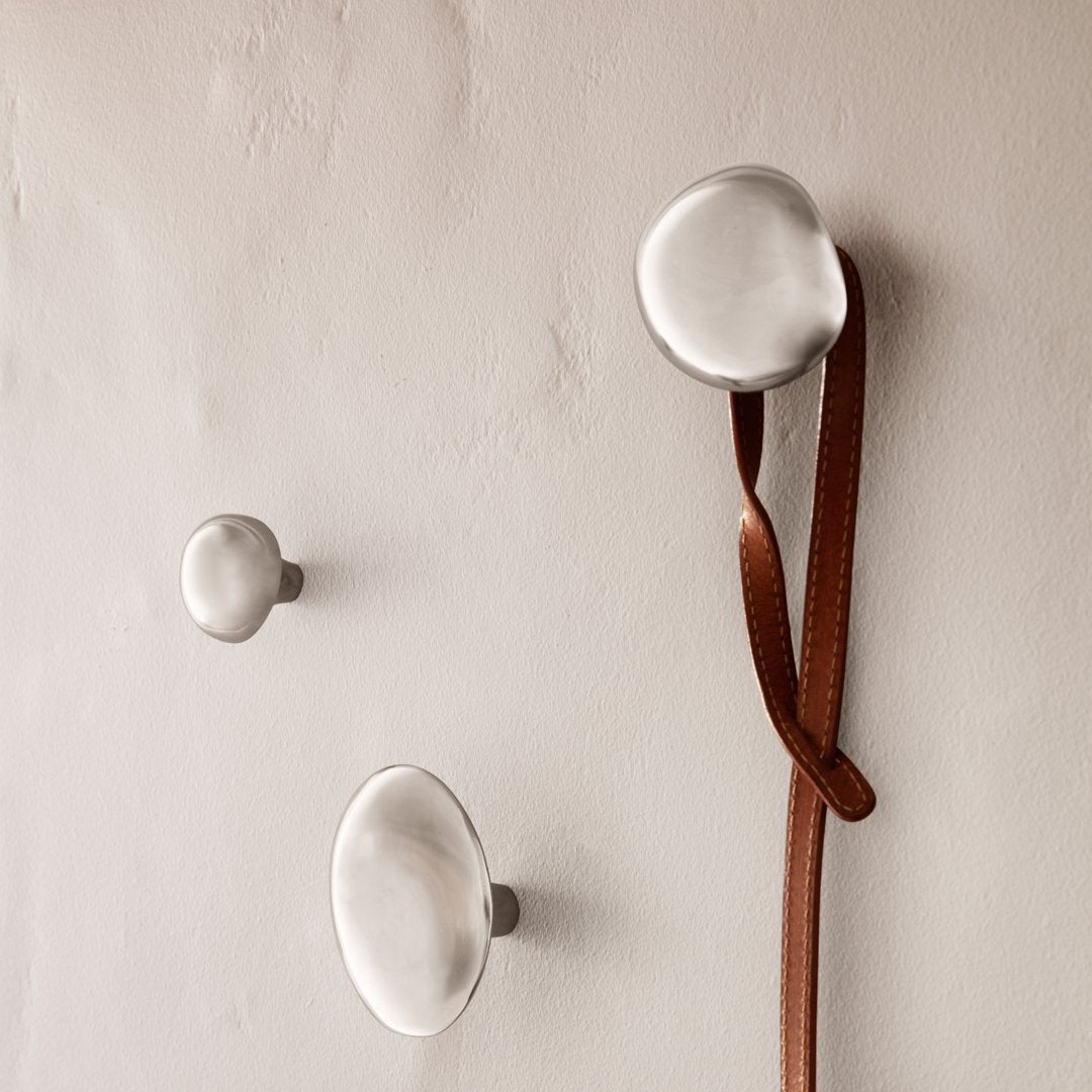 Sleek silver wall hooks in varying sizes, featuring a minimalist design against a neutral wall background.