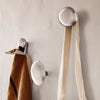 Sleek silver wall hooks against a neutral wall, showcasing smooth, rounded designs and earthy tones of the hanging items.