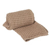 Soft beige waffle weave blanket, showcasing a textured grid pattern with rolled edge detail. Ideal for cozy decor.