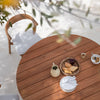 Round wooden table with a natural finish, complemented by soft gray seating and a neutral tableware set.