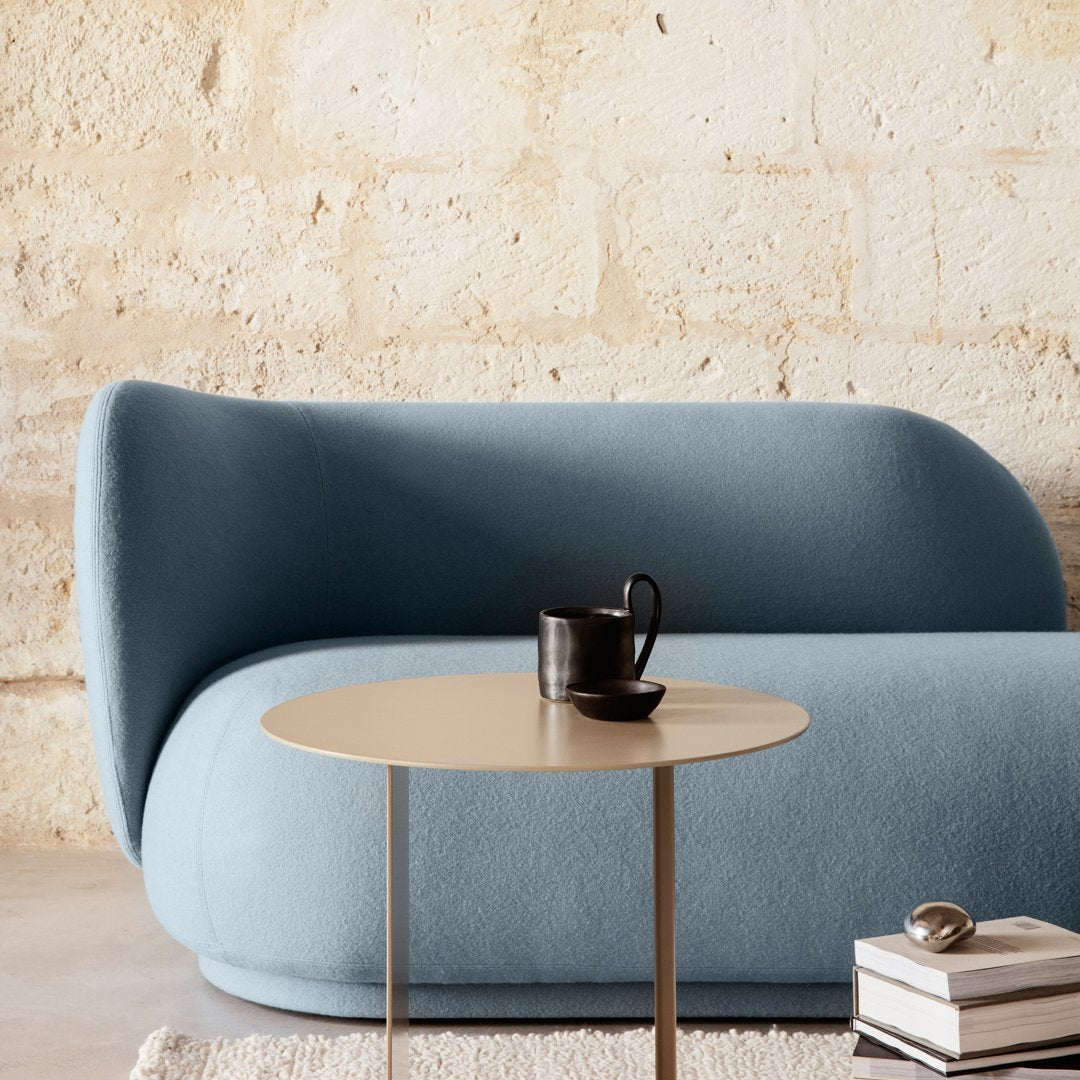 Soft blue curved sofa against a textured beige wall, with a sleek gold side table and monochrome decor accents.