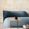 Soft blue curved sofa against a textured beige wall, with a sleek gold side table and monochrome decor accents.