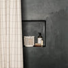 White grid-patterned shower curtain against a textured dark gray wall, featuring a white woven basket and dark accents.