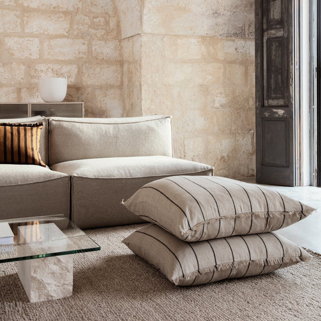 Neutral beige cushions with subtle striped patterns, styled on a textured natural rug in a warm, inviting living space.