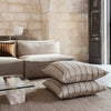 Neutral beige cushions with subtle striped patterns, styled on a textured natural rug in a warm, inviting living space.