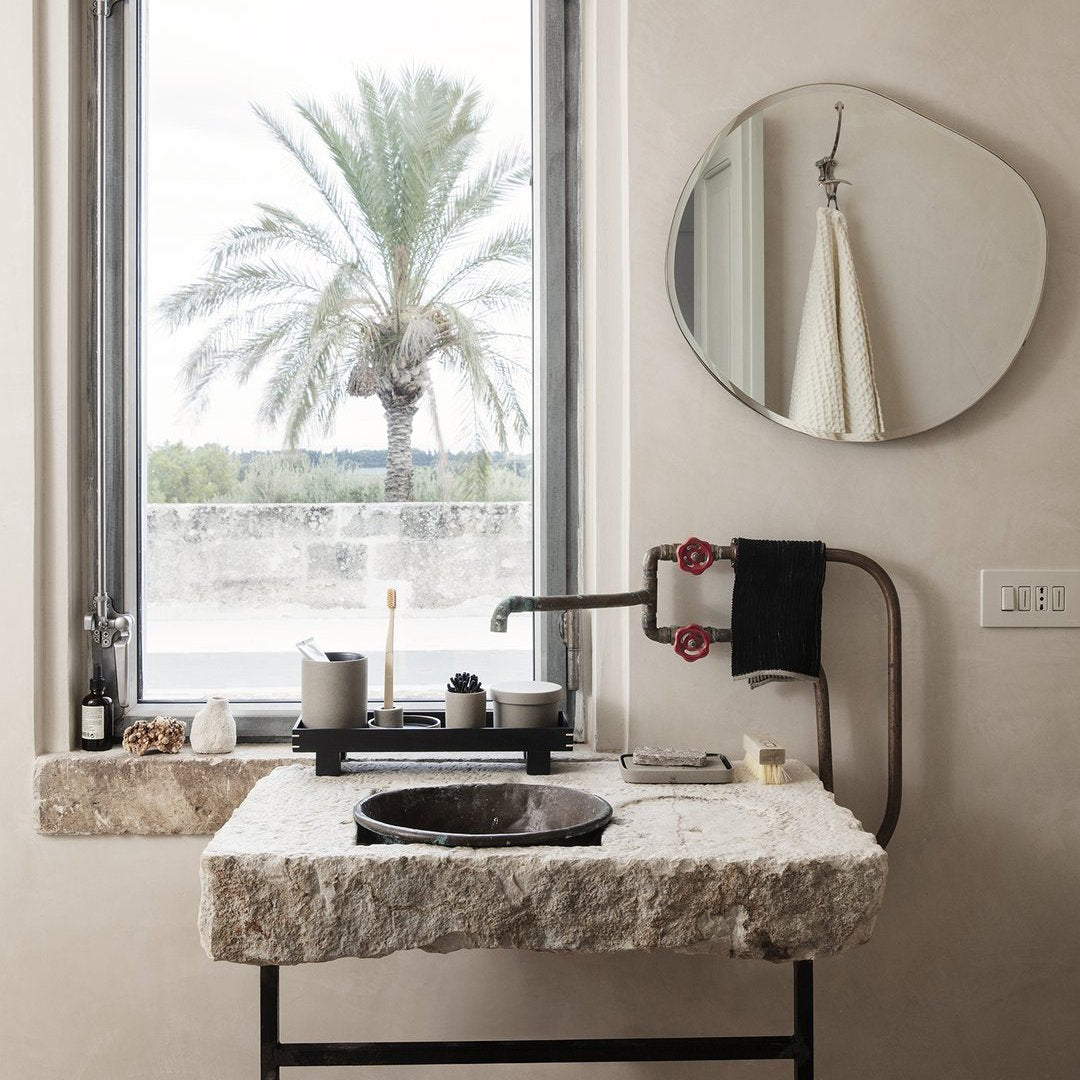 "Natural stone sink with a matte black bowl, earthy tones, and soft round mirror reflecting muted wall shades."