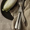"Neutral tones with a green accent from the lettuce, paired with vintage silver utensils on a textured linen backdrop."