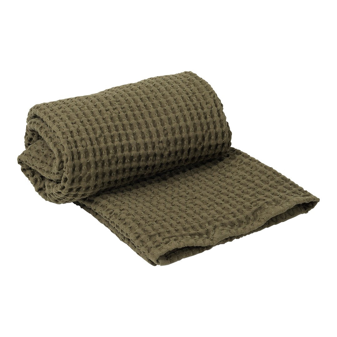 Olive green textured waffle weave towel, rolled and partially unfolded, featuring a cozy and stylish design.