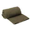 Olive green textured waffle weave towel, rolled and partially unfolded, featuring a cozy and stylish design.