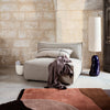 Gray modular chair with textured fabric, accented by a soft purple throw and a colorful abstract rug in earthy tones.