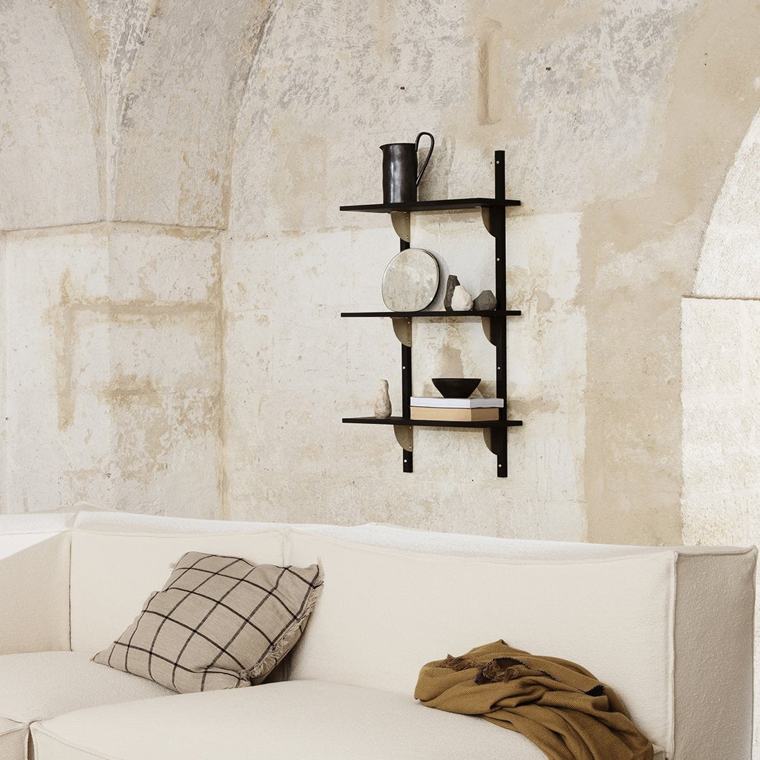Black metal shelf against a textured beige wall, with neutral-colored decor and a checkered cushion in soft tones.