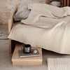Beige textured blanket layered over gray bedding, with soft woven patterns and a natural wood nightstand.