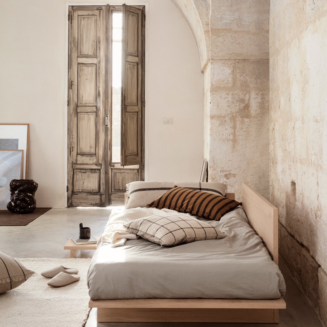 Neutral beige bedding with striped brown accents, complemented by a soft gray backdrop and natural wooden elements.
