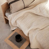 Beige textured blanket with a subtle grid pattern, paired with a neutral pillow and wooden bedside tray.