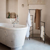 "Neutral beige and white towels hang on a sleek black rack in a minimalist bathroom with a stone bathtub."