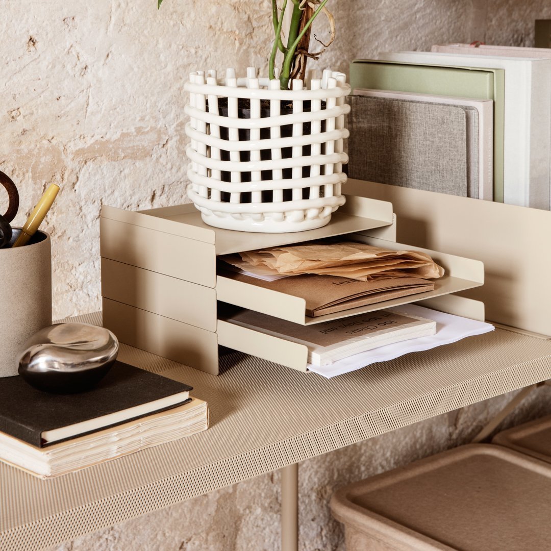 Beige desk organizer with layered drawers, paired with a white woven planter and neutral-toned stationery on a textured surface.