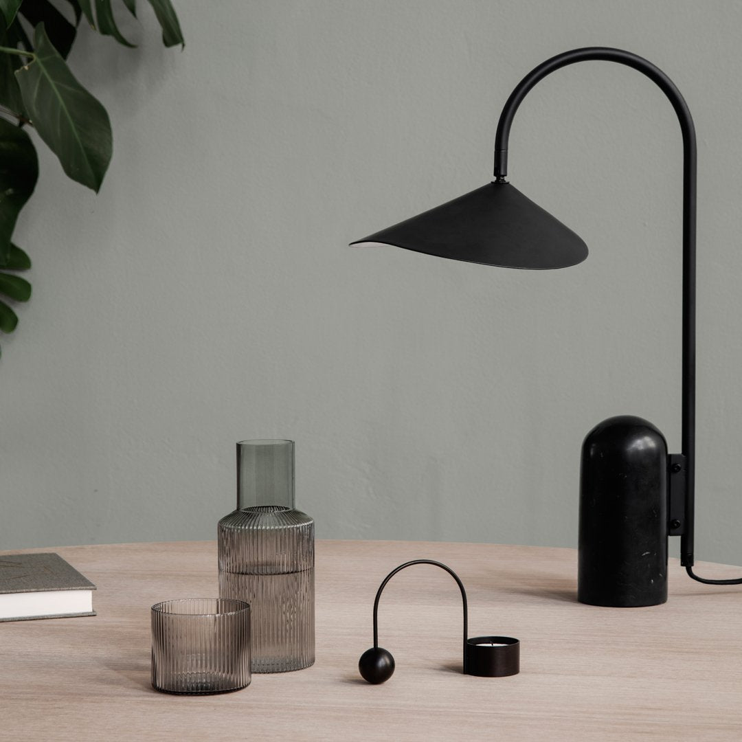 Stylish black lamp with geometric shades, glass vases in muted tones, and natural wood table. Modern decor essentials.