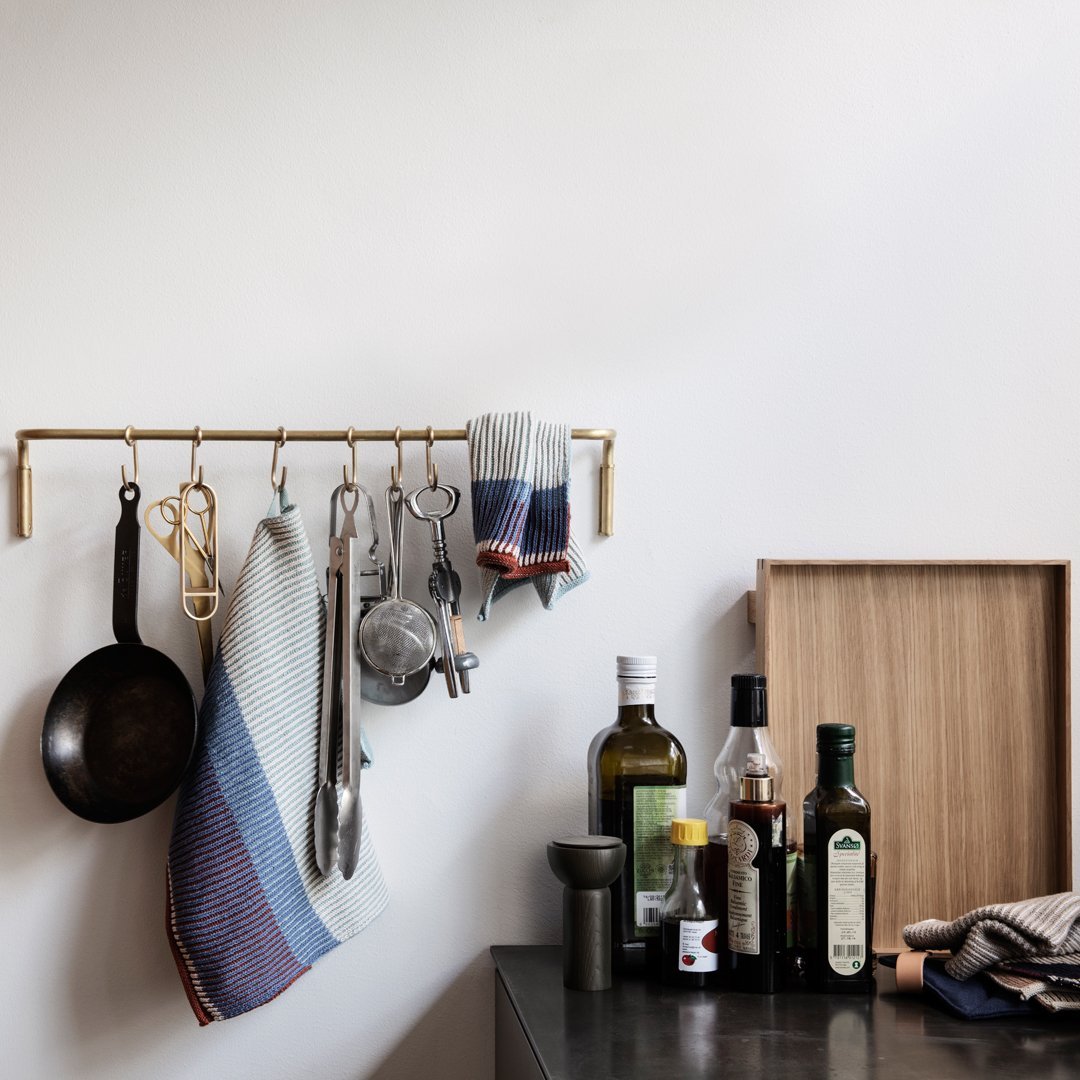Modern kitchen with teal and rust striped towels, brass rack, and dark olive oil bottles on a gray countertop.