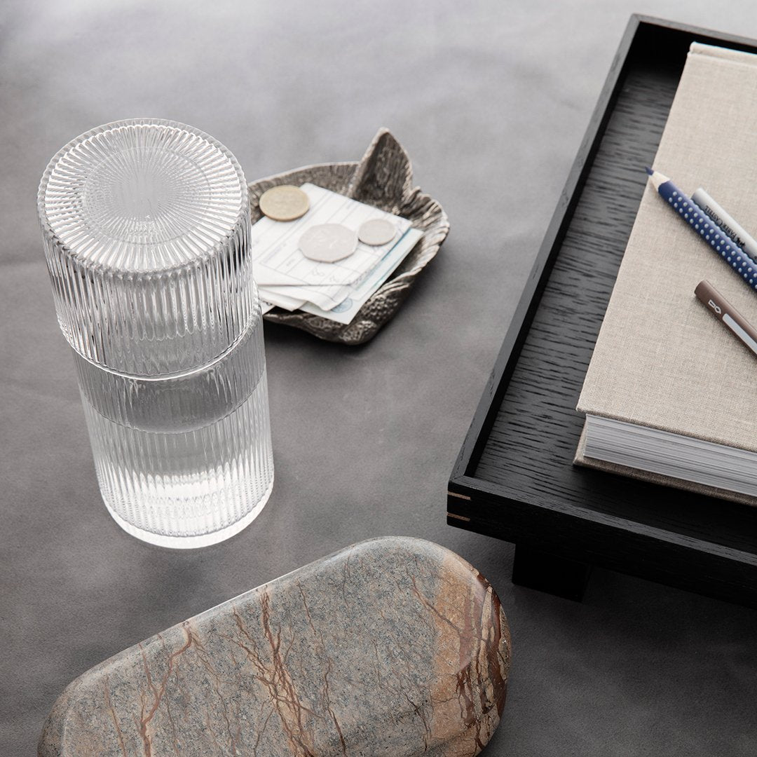 Clear ribbed glass tumbler on a textured gray surface with rustic stone and sleek black tray elements.